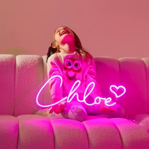 Girl sitting on sofa holding pink neon sign reading 'Chloe'